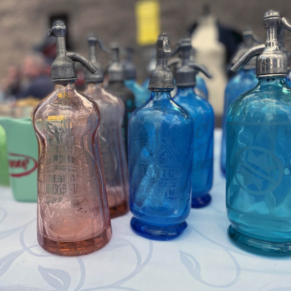 Alt text 1 Pink and blue glass antique vintage soda siphon bottles on a table at a flea market in France