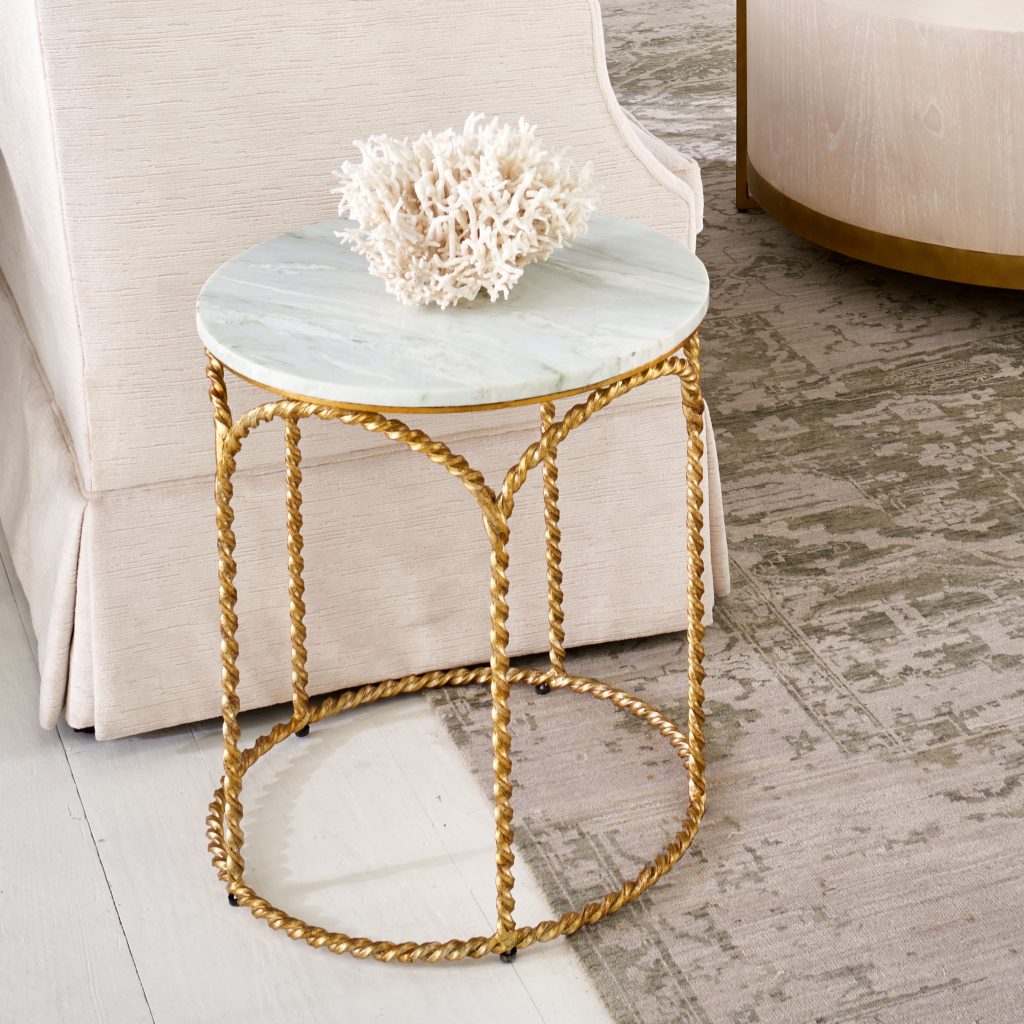 A pale room with an accent table with twisted metal rope legs and marble top. There is a large piece of white coral on the top of the table.