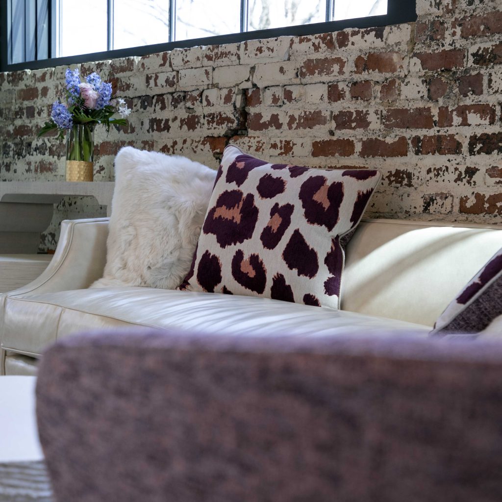 A distressed brick wall, white fabric settee, hyacinths in a vase and a spotted purple cushion
